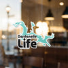 "Dardanelle Life" text on a teal abstract shape sticker on glass.