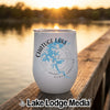 A white travel tumbler featuring a blue map of Chatuge Lake rests on a wooden dock overlooking a lake at sunset.