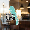Turquoise Winnipeg Life sticker on a glass window with blurred background.