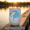 A white travel tumbler with a blue map of Lake Simcoe sits on a wooden dock at sunset.