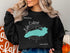 Black crewneck sweatshirt with a turquoise outline map of Lake Ontario.