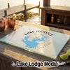 A glass cutting board rests on an outdoor wooden table, featuring a blue map of Lake Jocassee, South Carolina, and a compass design.