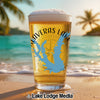 Beer glass with "Calaveras Lake Texas" map and compass design on beach.