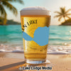 Glass of beer with "Glen Lake" and a blue map outline on a beach.
