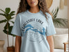 Light blue t-shirt with "FLAGSTAFF LAKE MAINE" text and lake outline over compass.