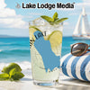 Glass with drink, limes, and mint on beach with sailboat and sunglasses.