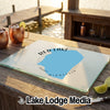 A glass cutting board with a blue map graphic of Red Lake, Minnesota, rests on an outdoor wooden table.