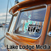 Teal "Minong Life" sticker on a wooden boat window, "Lake Lodge Media" text below.