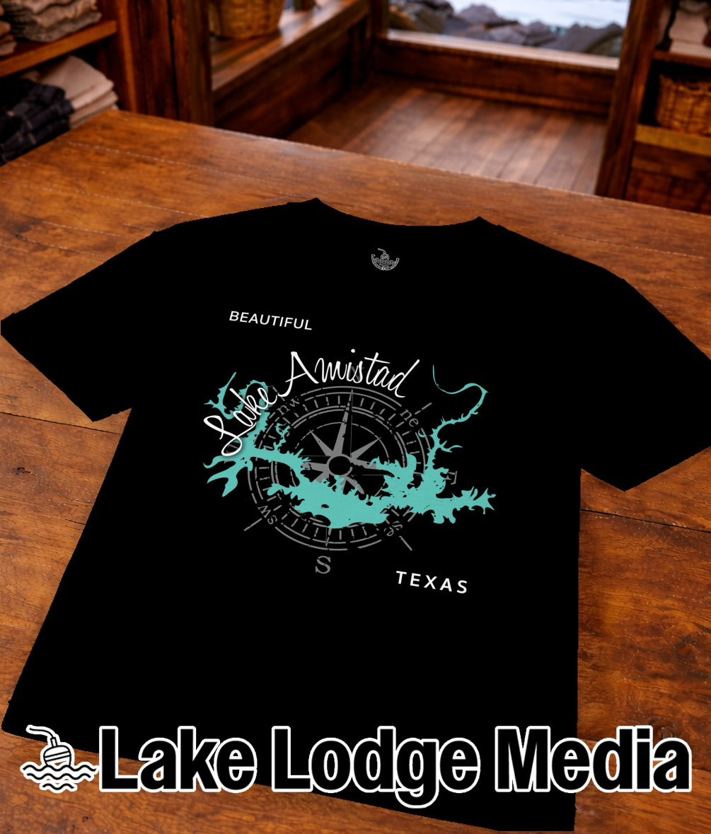 Black t-shirt with "Lake Amistad" and compass design on a wooden table.
