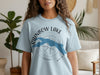 Light blue t-shirt with "Rainbow Lake Maine" text and a blue lake shape overlayed on a compass.