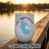 A white insulated wine tumbler featuring a blue map of Lake Tohopekaliga and black text sits on a wooden dock at sunset.