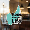 Teal shape sticker with black text "Rose Canyon Life" on a window.