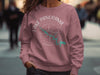 Woman wearing dusty rose sweatshirt with "Lake Panorama Iowa" compass graphic.