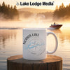 White mug with Norris Lake, Tennessee design and compass on a wooden post by a lake.