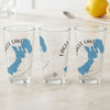 Three clear pint glasses on a marble countertop, each printed with a blue map and compass design.