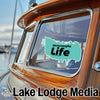 Teal McConaughy Life sticker on a wooden boat window with "Lake Lodge Media" text.