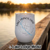 A white insulated wine tumbler with a compass and lake design sits on a wooden dock at sunset.