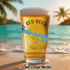 Glass of beer with "Lake Red Rock" and a blue map graphic on a beach.
