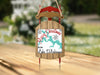 Christmas ornament shaped like a red and wood sled with text.