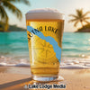 Glass of beer with "ALUTNA LAKE" text and compass design on beach