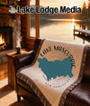 Woven blanket with Lake Mascuppic outline on a couch by a fireplace.