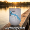 A white stemless wine tumbler rests on a wooden dock with a lake sunset in the background.