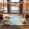 Glass cutting board featuring a map of Lake Monticello, South Carolina, surrounded by crackers, cheese, and fruit on a wooden table.
