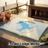 A rectangular glass cutting board with a blue Lake Siskiyou map design rests on a wooden table outdoors.