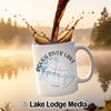White mug with "Rough River Lake" and compass design, coffee pouring in.