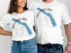 White t-shirts with Eklutna Lake map and compass design, "Alaska" text.
