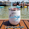 A white insulated tumbler featuring a Lake Spivey Georgia compass design rests on a wooden dock with boats and people in the water.