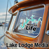 Teal lake graphic with Monroe Life text on boat window, Lake Lodge Media logo below.