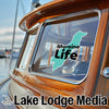 Teal outline of a dog with "Moraine Life" text on boat window, "Lake Lodge Media" text below.