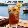 Glass of iced tea with "Burnsville Lakes" design and lemon slice by a lake.