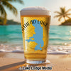 Glass of beer with "Flathead Lake" map and compass design, on a beach.