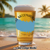 A pint glass filled with beer stands on a sunny beach, featuring a blue outline graphic and Lake McConaughy Nebraska text.