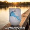 A white insulated wine tumbler featuring a blue lake silhouette and compass design resting on a wooden dock.