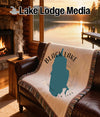 Woven blanket with Black Lake map and New York text draped on a leather sofa.