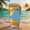 Glass of beer with "Emerald Lake" and map graphic on beach background.