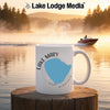 White mug with "Lake Mary Minnesota" map design and steaming coffee, lakeside.