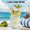 Glass with drink, lime, mint, and sunglasses on beach with sailboat.