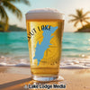 Glass of beer on a beach with palm trees and ocean waves.