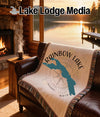 Woven blanket with Rainbow Lake Maine map and compass design on a leather sofa.