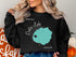 Black sweatshirt with "Beautiful Crater Lake Oregon" graphic in teal and white.