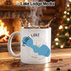 White mug with "Pearl Lake Wisconsin" design, steaming coffee, fireplace, and Christmas tree background.