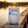 A white insulated tumbler featuring a Lake Rayburn, Arkansas map and compass design sits on a wooden dock at sunset.