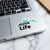 Weiss Life sticker on a laptop keyboard with a blue lake outline.