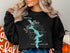 Black sweatshirt with a turquoise Lake Lyman map and compass design.