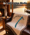 Woven blanket with Conesus Lake map and compass design on leather couch.
