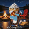 Drink with whipped cream and ice in front of campfire, lake, and chairs.